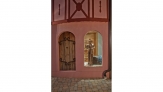 A silver knight stands holding his sword upright in a window beside a wooden door on this unique pink house