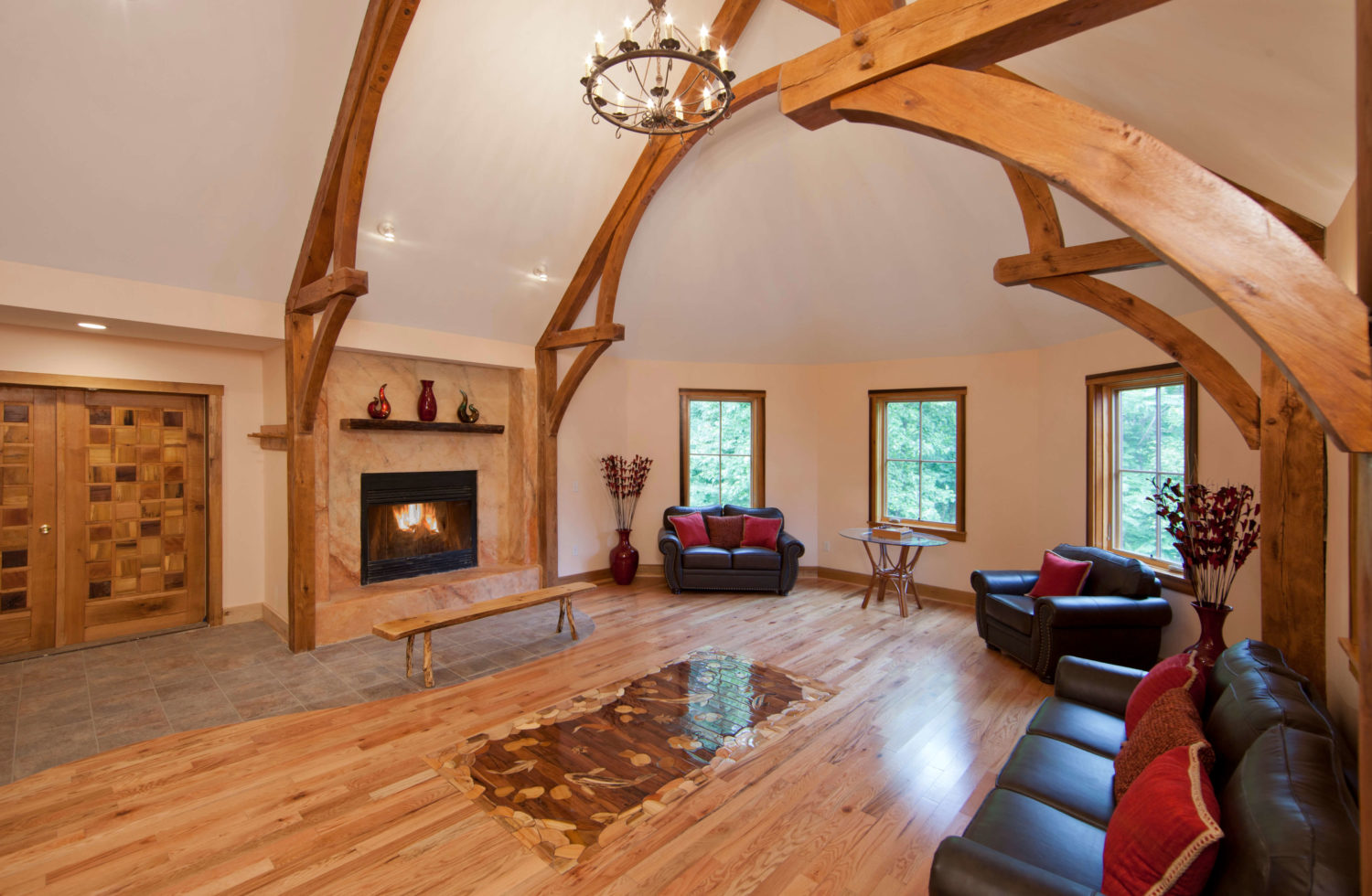 lobby with fireplace and arching wooden beams and several dark browncouches with red throw pillows surround the room