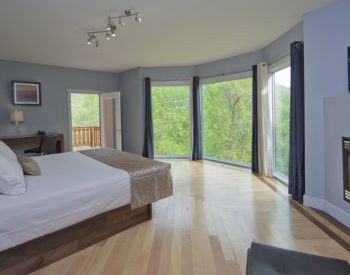 Light shines through the huge windows across the hard wood floors onto the beautifully made white bed