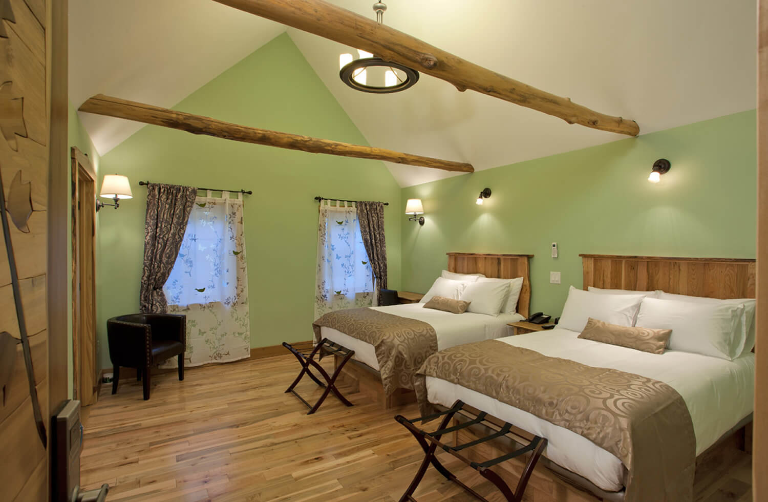 A natural green room with tan accents has two white beds with tan throw blankets