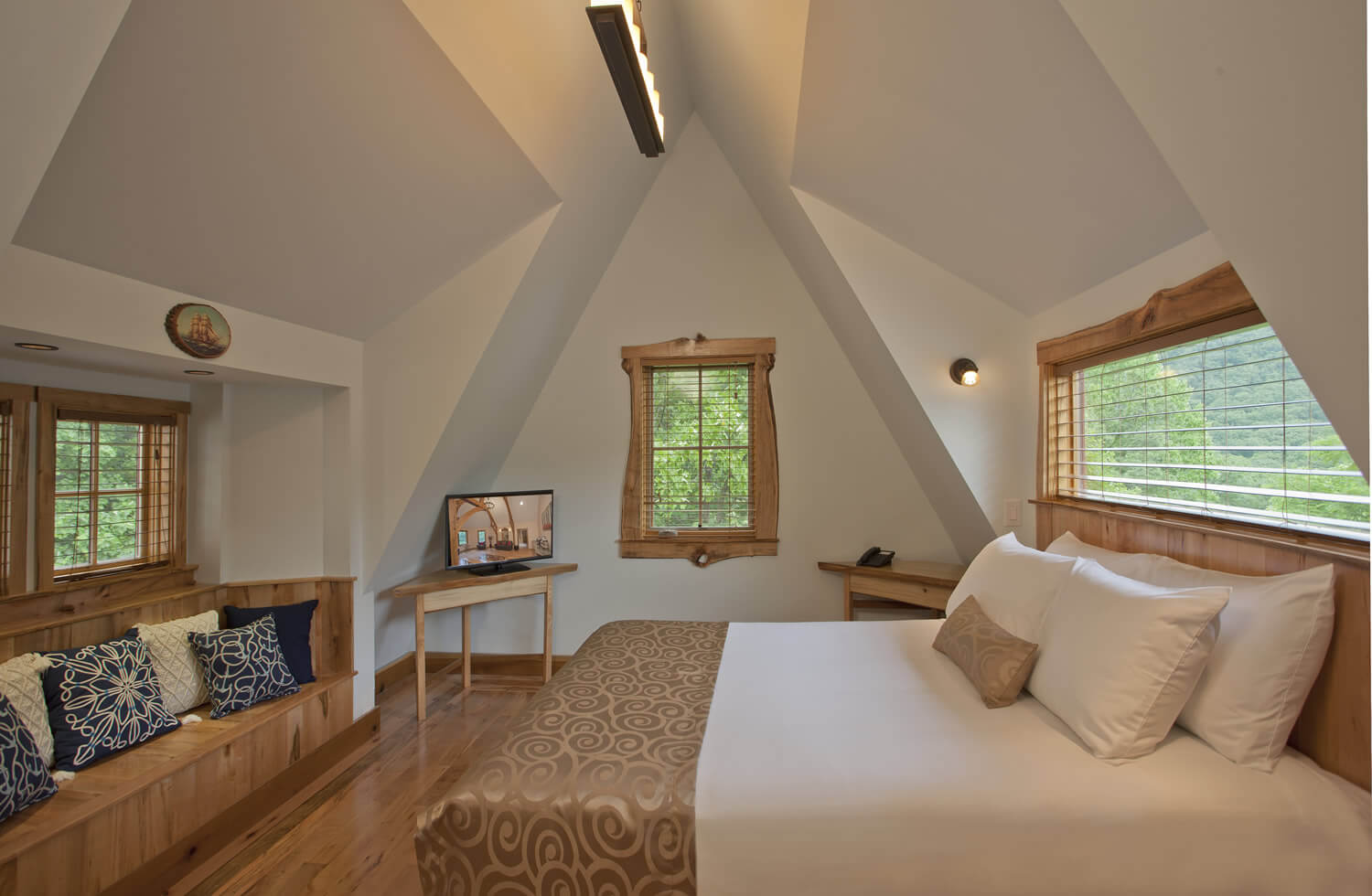 Cozy room with light blue walls and steep sloped roof. One queen bed and build-in bench with many soft pillows.