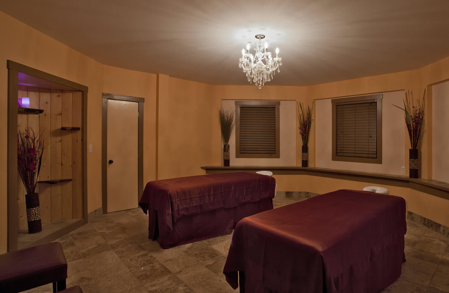 octagonal room with large windows and chandelier. Two massage tables with burgundy satin sheets in the middle of the room.